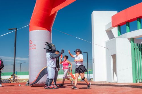 Runners celebrate with high fives at a marathon finish line under a clear blue sky.